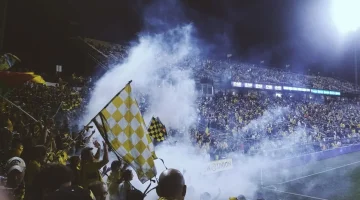 A vibrant stadium filled with cheering fans focusing on the screen where a football match